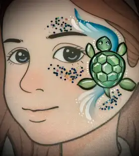 Sea turtle face painting design beside the eye with blue-green shell details and bubbles.