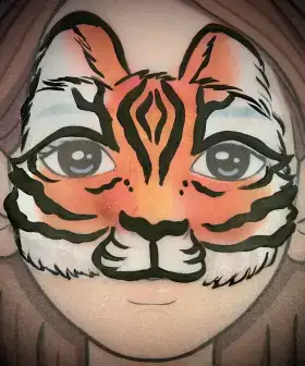 Orange tiger face painting mask with black stripes and white muzzle details around the eyes.